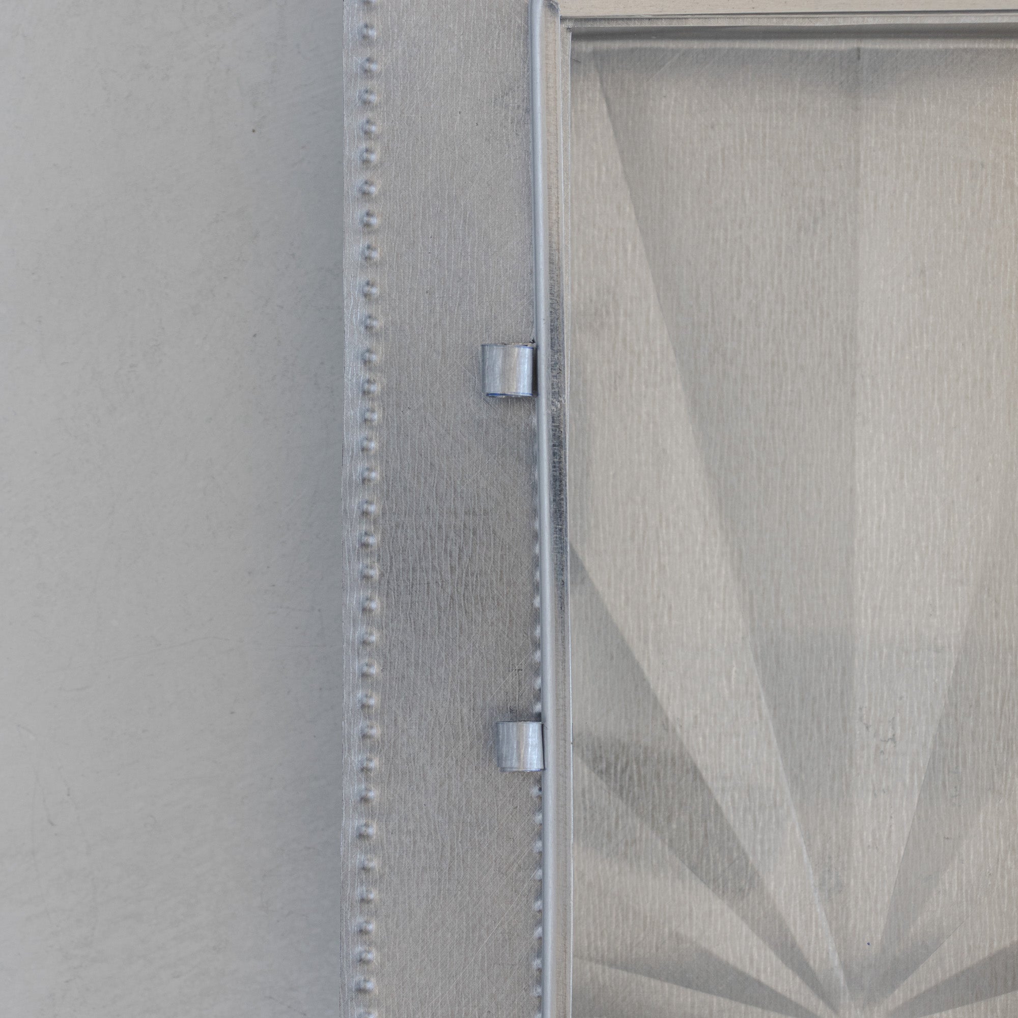 Close-up of Nicho de Recuerdo showing the hand-formed tin door handle and dot-punched edge detail on the left side panel, glass door visible at right.