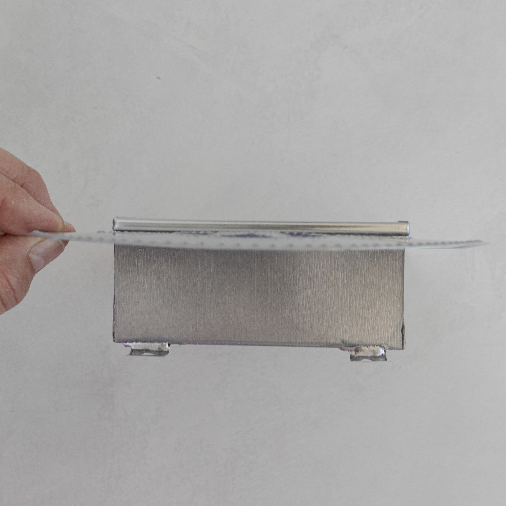 Top profile of Nicho de Recuerdo held by hand, showing the depth of the tin box construction and hanging wire.