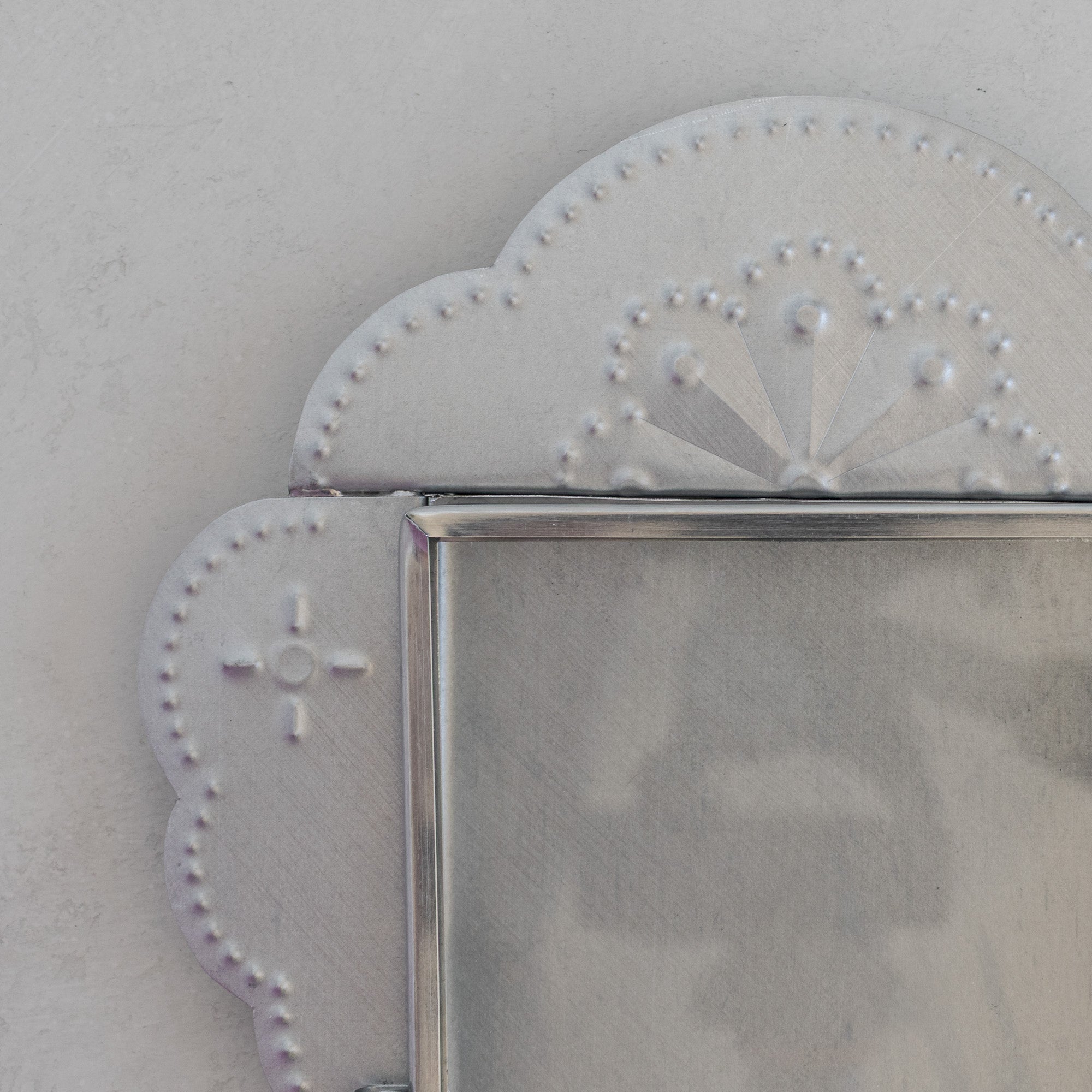 Close-up of Nicho Postal crest showing hand-punched fan motif and dot-punched cloud form in natural tin, with glass door frame visible below.