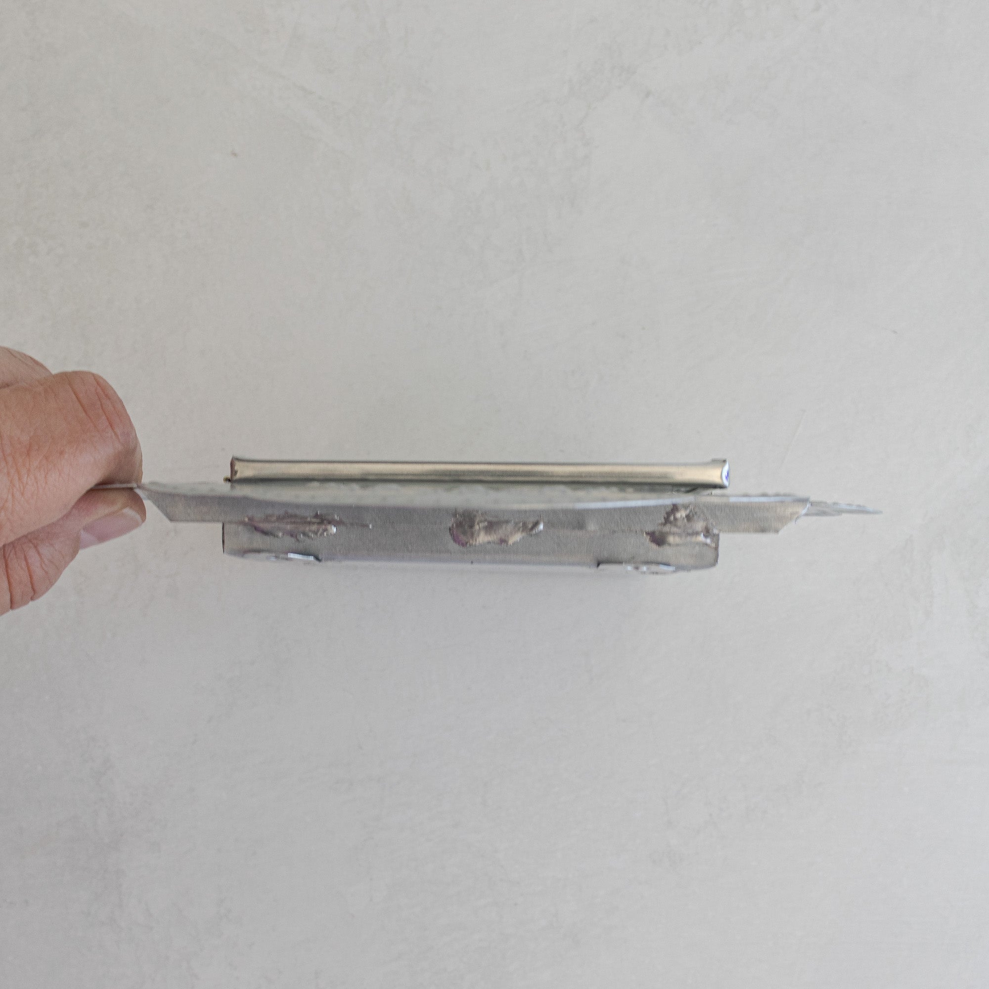 Top profile of Nicho Postal held by hand, showing the shallow depth of the tin box construction.