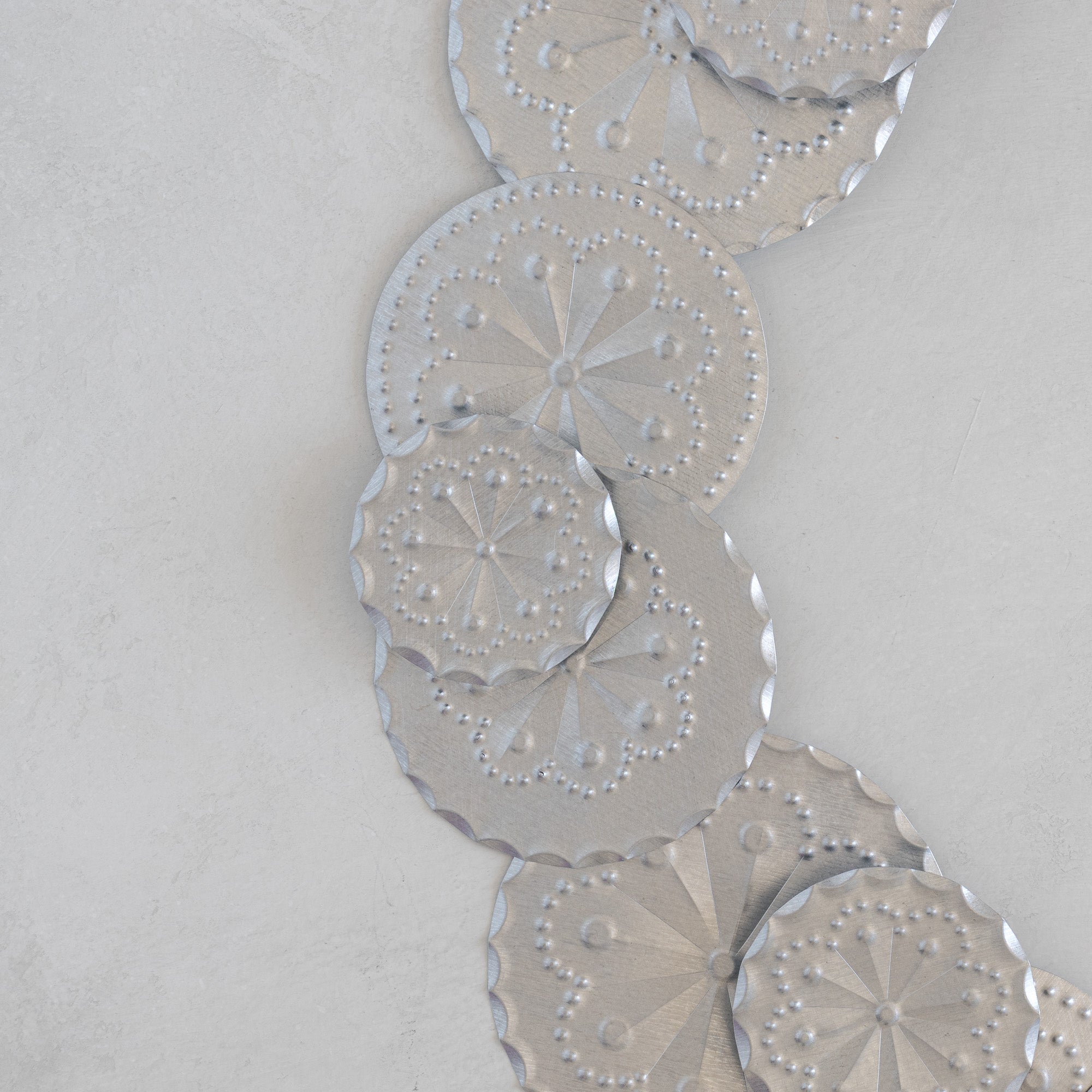 Close-up detail of Roseta Corona tinwork wreath showing hand-punched rosette disc motifs and crimped edges in natural tin.