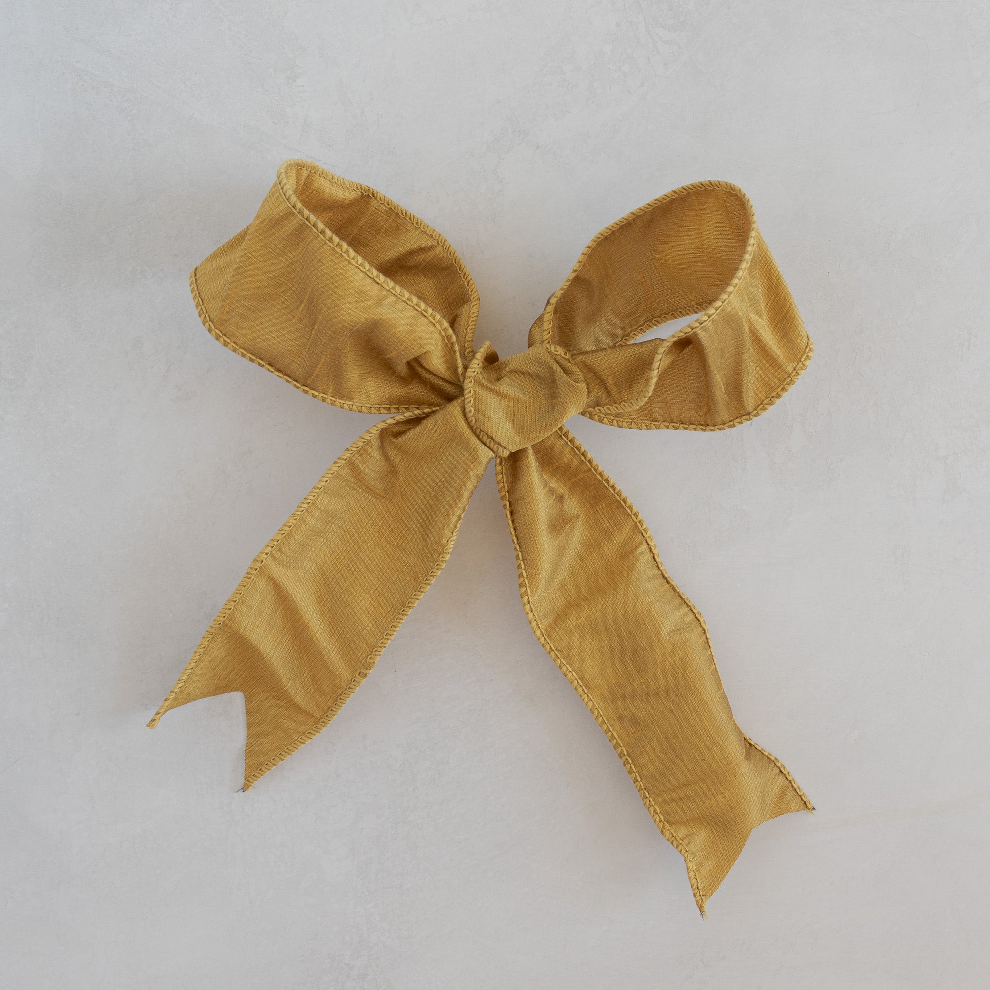 Gold dupioni ribbon bow for Roseta Corona, photographed flat on a light plaster surface.
