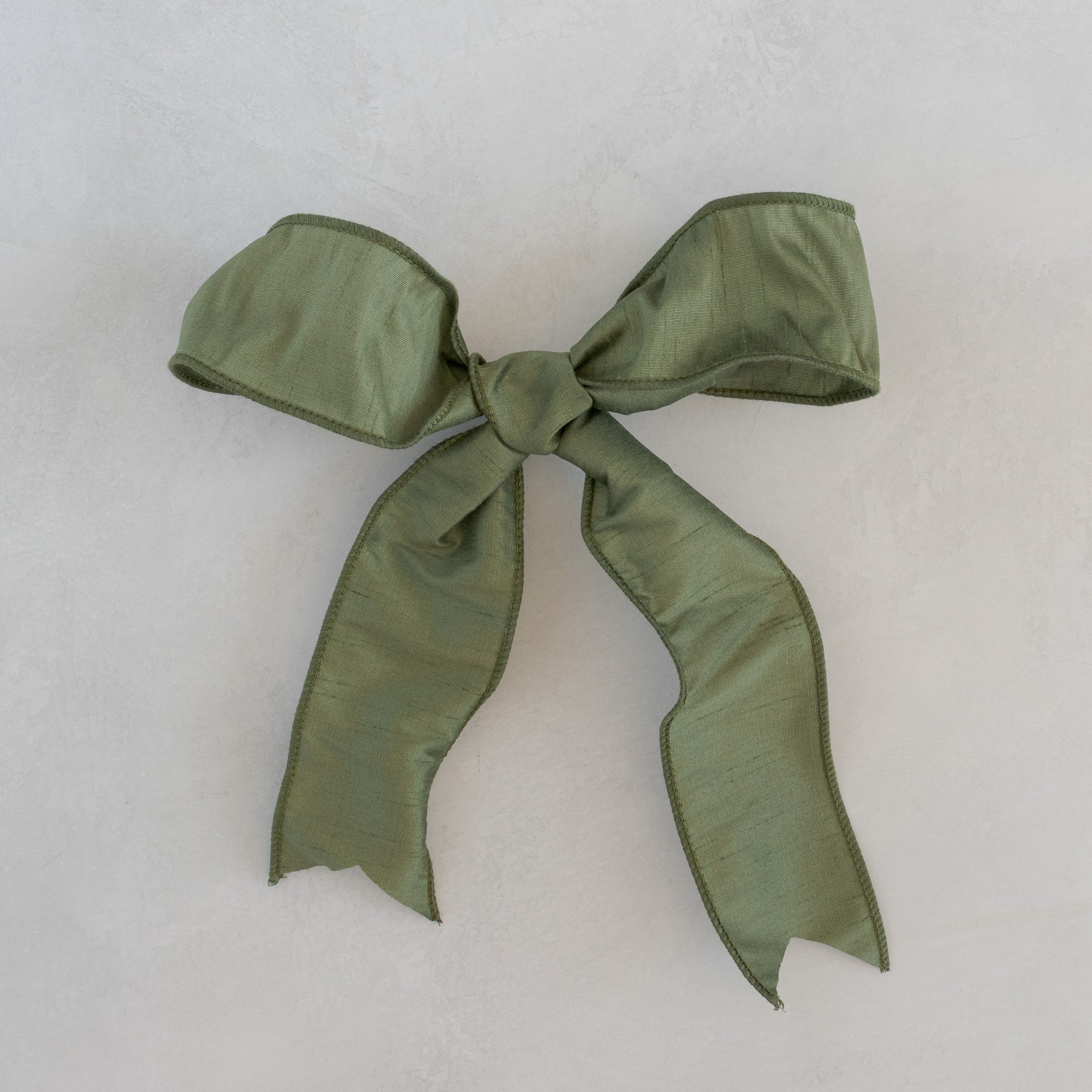 Moss dupioni ribbon bow for Roseta Corona, photographed flat on a light plaster surface.
