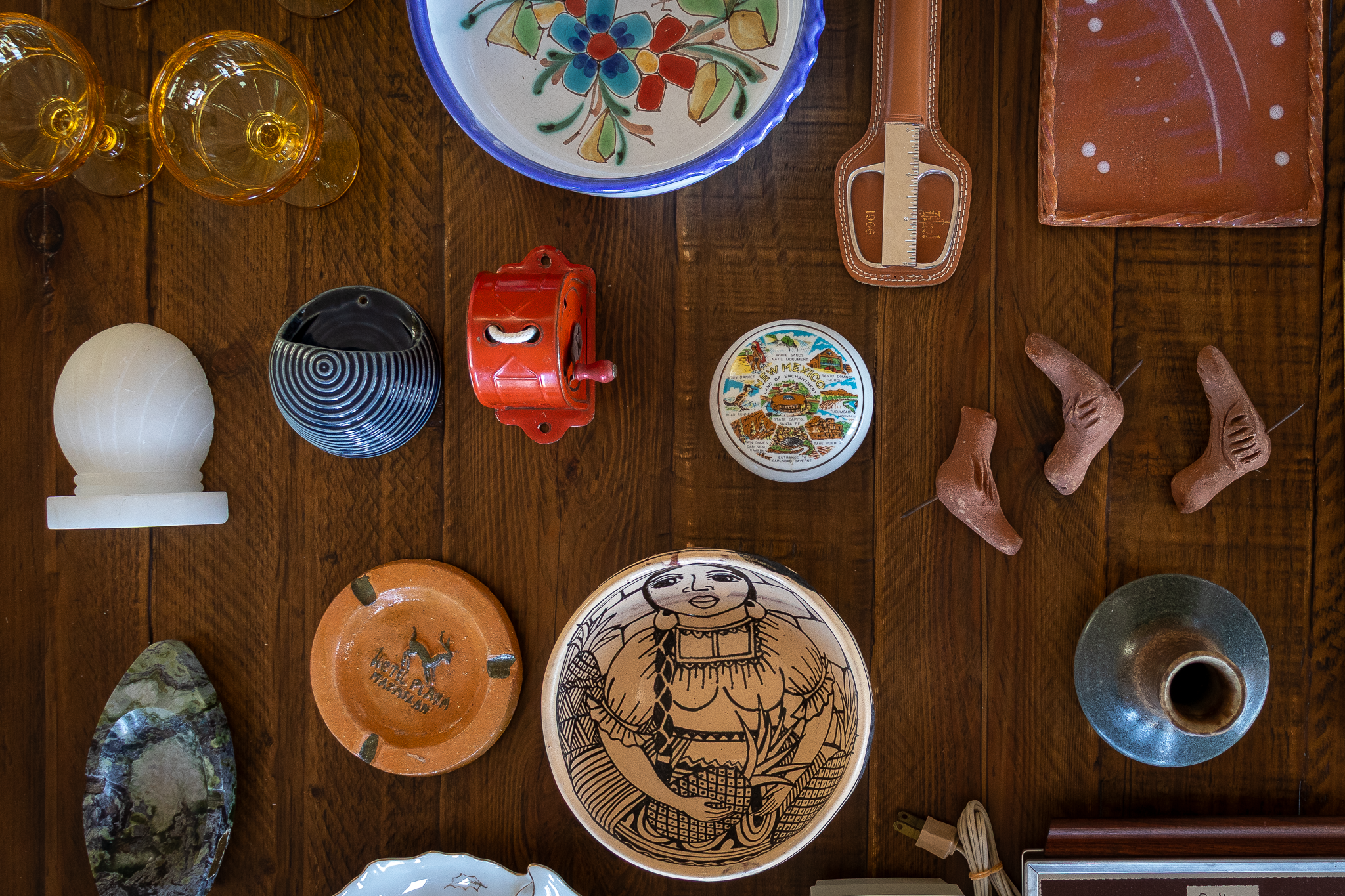Flat lay of assorted vintage and secondhand home goods arranged on a wooden table, including pottery, ceramics, glassware, and decorative objects in warm earthy tones.