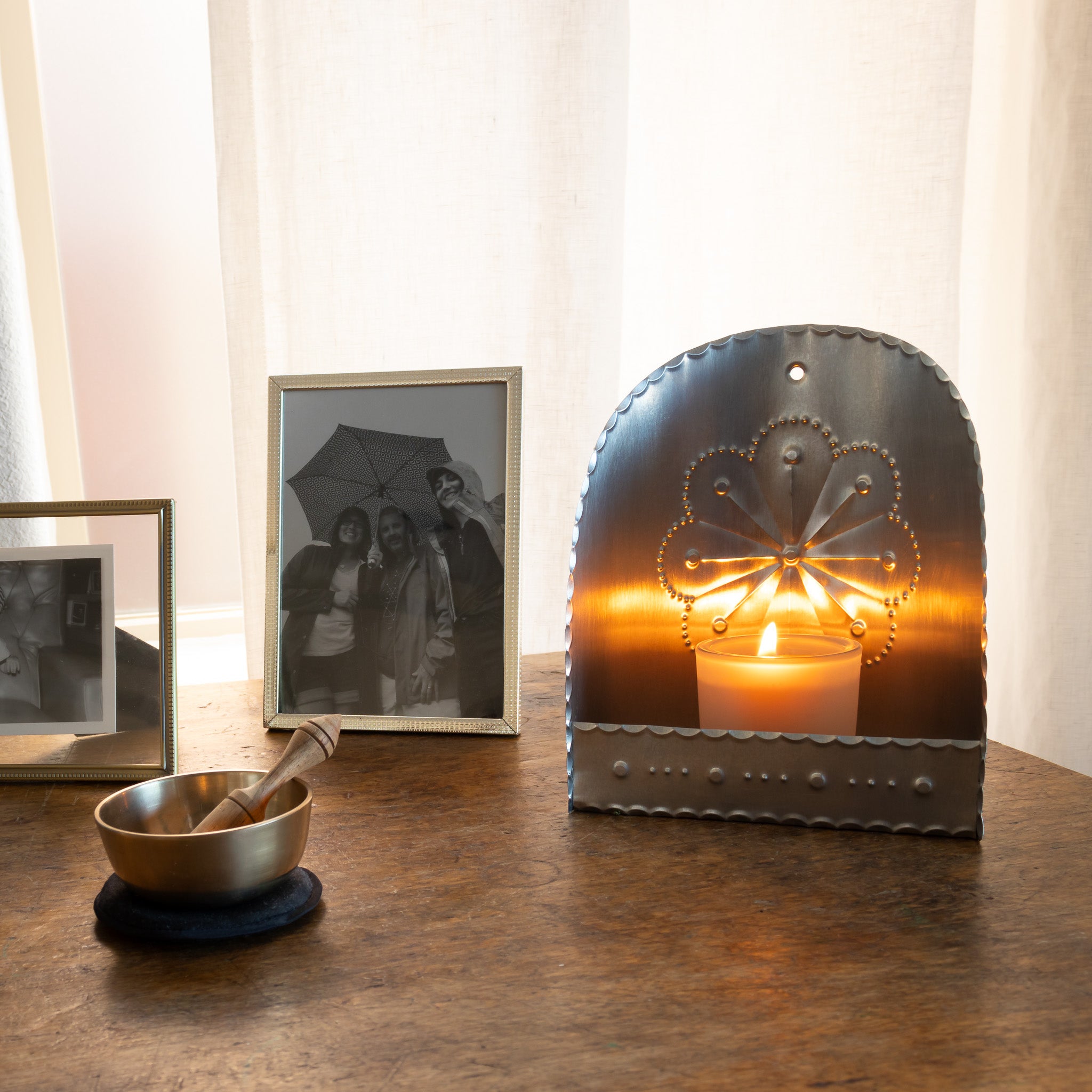 Handmade tin candleholder with a lit candle on a table in a home setting